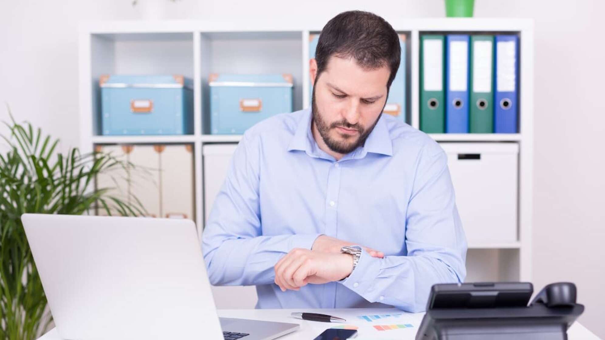 Mann im Büro blickt auf seine Uhr