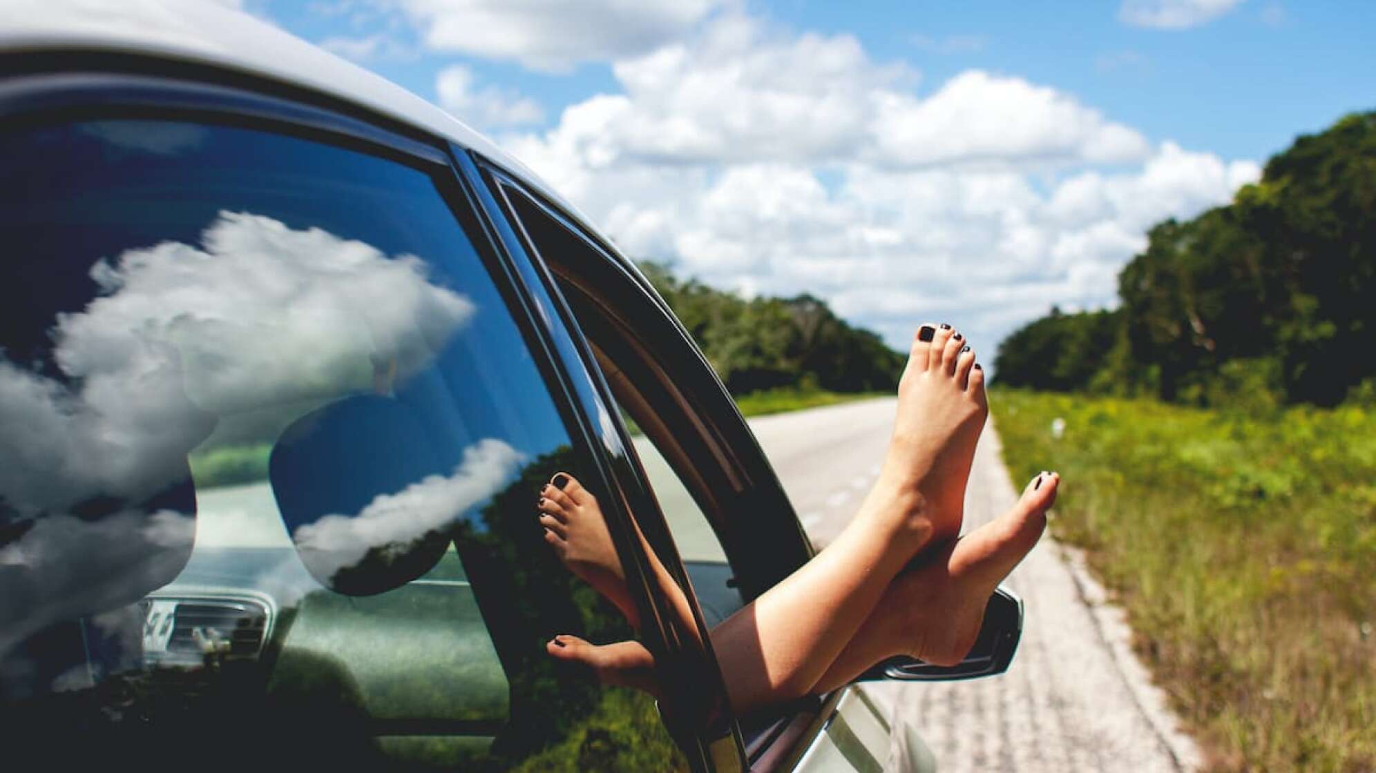 Eine Frau hängt ihre Füße aus dem Autofenster.